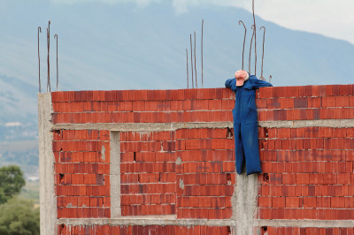 Eine als Bauarbeiter verkleidete Puppe hängt an frisch gemauerter Hausfassade ohne Dach