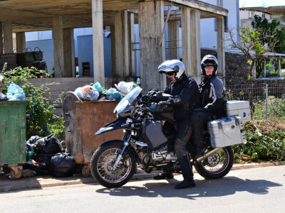 Motorradfahrer mit Beifahrerin vor Müllcontainer