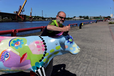 Mann packt Hörner einer Kuh aus Plastik im Hafen von Ventspils