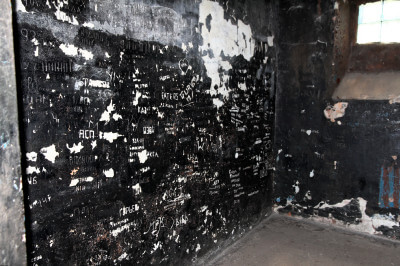 Eingeritzte Hinweise der ehemaligen Insassen sind an der schwarzen Wand noch gut lesbar.