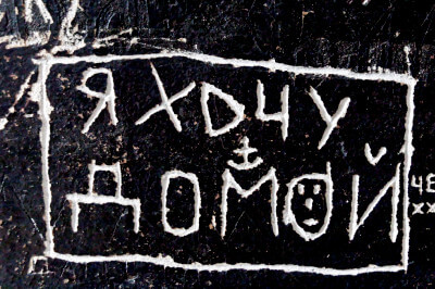 Detailaufnahme der Wand mit den eingeritzten Hinweisen. Der Text dieses Hinweises heißt übersetzt: Ich will nach Hause!