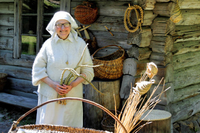 Eine ältere Dame mit Häubchen flechtet aus Stroh Körbe, Ruten, Unruhen und Glücksbringer.