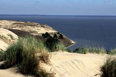 Blick über Sanddünen mit Grasbüschel auf das offene Meer