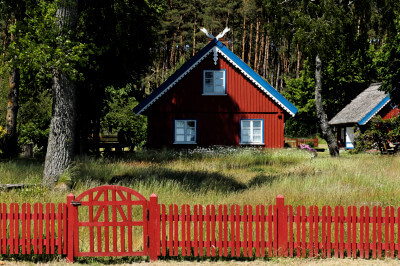 Braun gestrichenes Holzhaus mit blauem Dachabschluß und rotem Zaun im Vordergrund