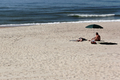 Mann sitzt unter Sonnenschirm am leeren Strand