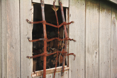 Verrostetes Gitter vor Fenster an einem Holzhaus