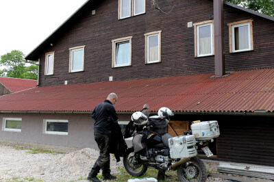 Motorradfahrer bepackt sein Motorrad vor Holzhaus