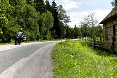 Motorrad fährt auf Straße an Holzhaus vorbei