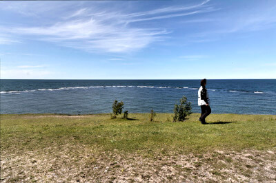 Frau steht vor Klippe im Hintergrund das offene Meer