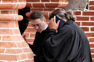 Zwei Geistliche beim Eintritt ins Kloster, einer davon mit Handy am Ohr