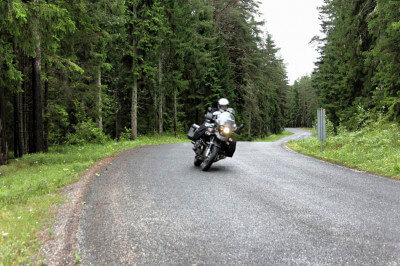 Motorrad fährt in Schräglage auf bewaldeter Straße im Lahemaa-Nationalpark