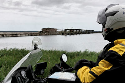 Motorradfahrer blickt auf die im Hintergrund liegenden reste der geheimen U-Boot-Station Hara