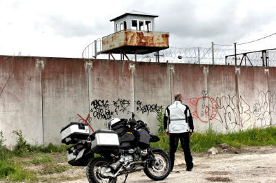 Motorrad steht vor verfallenem Gefänginszaun mit Aussichtsplattform in Rummu Quarry
