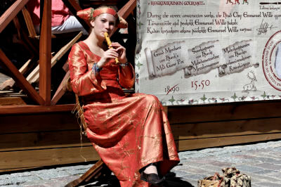 In mittelalterlicher Tracht gekleidete Frau sitzt auf einer Flöte musizierend in der Altstadt von Tallinn