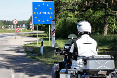 Motorradfahrer steht vor Grenzschild zu Lettland
