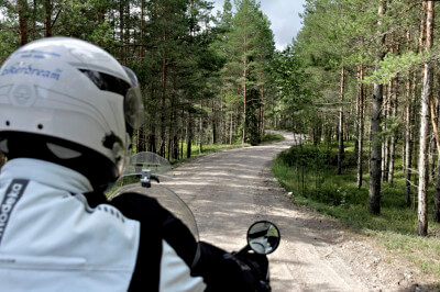 Motorradfahrer steht auf offroad Weg durch Nadelwald
