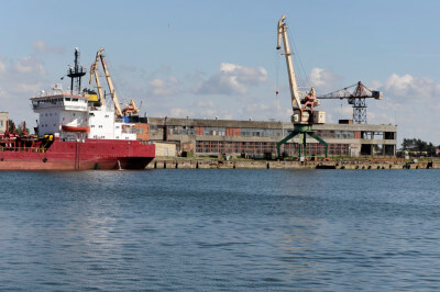 Schiff liegt in Hafenanlage vor Anker. Im Hintergrund Entladekähne.
