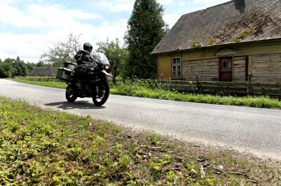 Motorrad fährt an altem Holzhaus vorbei