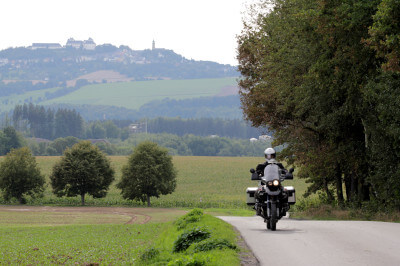 Motorrad fährt auf Straße. Im Hintergrund die Augustusburg.