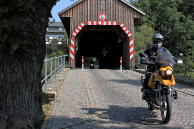 Motorrad fährt aus gedeckter Holzbrücke in Hohenfichte