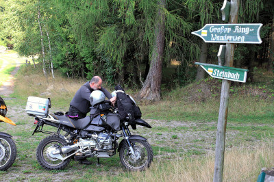 Motorradfahrer auf Parkplatz im Wald vor Hinweisschildern