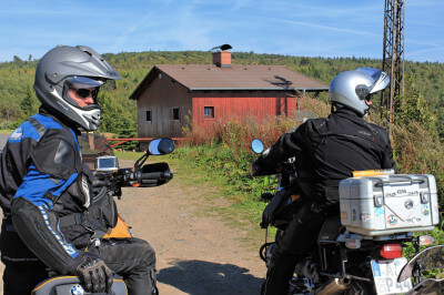Zwei Motorradfahrer vor Hütte blicken rückwärts