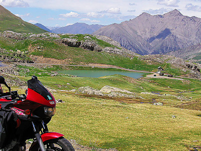 Motorradfahrer steht vor Landschaft mit kleinem See und Bergen
