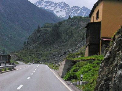 Straße mit Motorradfahrer und Haus bei der Auffahrt zum Flüelapass
