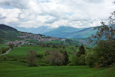 Grüne Wiesen und im Hintergrund ein Dorf am Monte Baldo