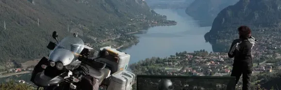 Motorradtouren zwischen Gardasee und Idrosee - Blick auf den Idrosee. Unten rechts Idro, hinten links Anfo, wo sich der Einstieg zum Pso. Spina, Maniva etc. befindet. Frau mit Motorrad steht hoch über dem Idrosee und blickt hinunter