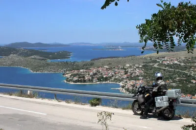 Kroatische Küstenstraße Motorradfahrer vor Leitplanke dahinter blaues Meer mit Bergen