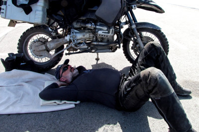 Motorradfahrer liegt im Schatten seines Motorrades auf einer Decke und schläft