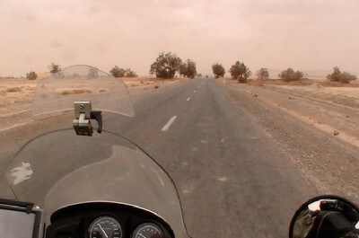 Motorrad fährt über Straße in karger Landschaft mit Sand Verwehungen