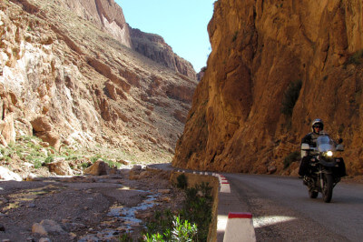 Motorrad fährt auf rechter Seite entlang der steil aufwachsenden Felsen der Todra-Schlucht
