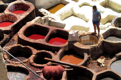 Mann steht vor etlichen verschieden farbigen gemauerten Farbtöpfen in der Ferberei in Fes