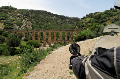 Im Hintergrund ein römisches Äquadukt in der bergigen bewachsenen Landschaft