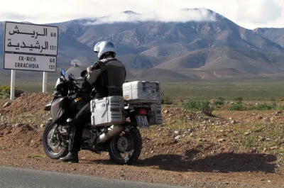 Der Hohe Atlas grüßt in der Ferne. Motorrad steht vor Straßenschild