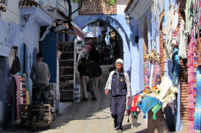 Marokaner läuft durch Einkaufsgasse mit Tüchern in Chefchaouen