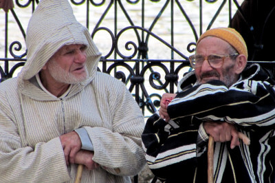 Zwei in traditionellen Gewänder gekleidete Marokkaner sitzen im Gespräch vertieft vor einem schwarzen Geländer