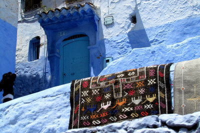 Blau weiß gestrichenes Haus mit Türe und vorne an ein gemusteter Teppich zum trocknen