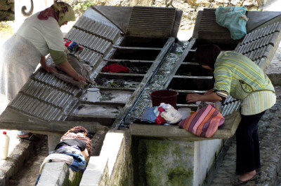 Blick auf die öffentliche Waschstation mit gerillten Steinobeflächen und Frauen bei der Wäsche in Chefchaouen