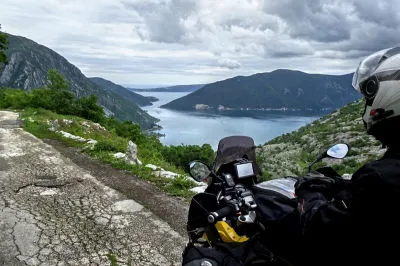 In 550 Meter Höhe über dem Meer beginnt eine etwa anderthalbspurige Straße, die hinunter nach Risan in der Bucht von Kotor führt. Motorradfahrer blickt über die Bucht von Kotor mit Inseln und blauem Meer von oben