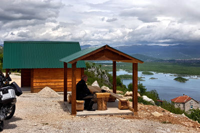 Kleine Holzhütte an einem Parkplatz mit Motorrad und Blick auf den Slano-Stausee