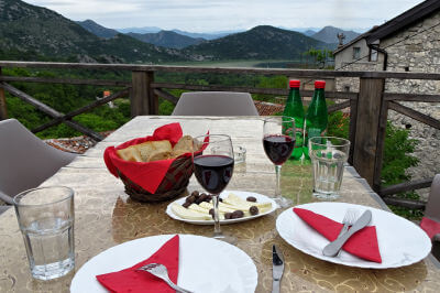 Tisch gedeckt mit Tellern mit Messer und Gabel, einem Brotkorb und zwei Gläsern Rotwein mit Panoramablick über den Skadarsee