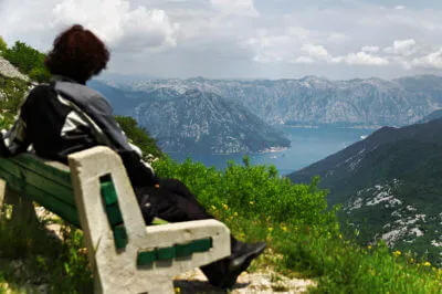 Motorradfahrerin sitzt auf einer Bank mehrere hundert Meter über der Bucht von Kotor