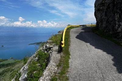 Straße an steiler Felswand mit kleiner gelben Leitplanke und Blick übers Meer
