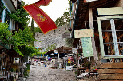 Blick die Gasse hinauf entlang der Restaurants mit einer montenegrinischen Fahrne in Stari Bar