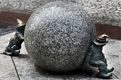 Zwei Zwerge aus Bronze rollen eine riesige Kugel