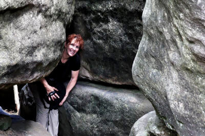 Frau mit Kamera in der Hand schaut aus einer Felsspalte heraus
