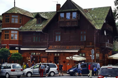 Dorfidylle mit großem Holzhaus mit parkenden Autos in Zakopane
